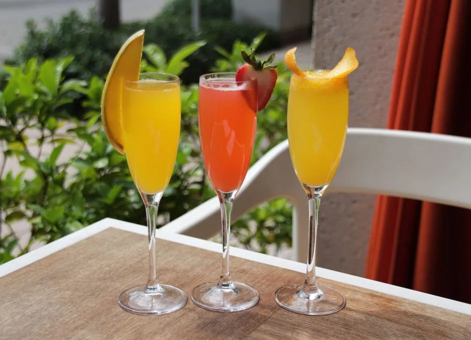Three vibrant fruit mimosas with garnishes on an outdoor table