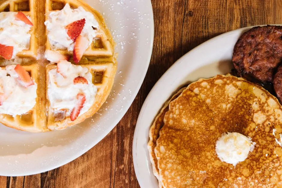 Plate of pancakes, waffles, and sausages topped with whipped cream and strawberries